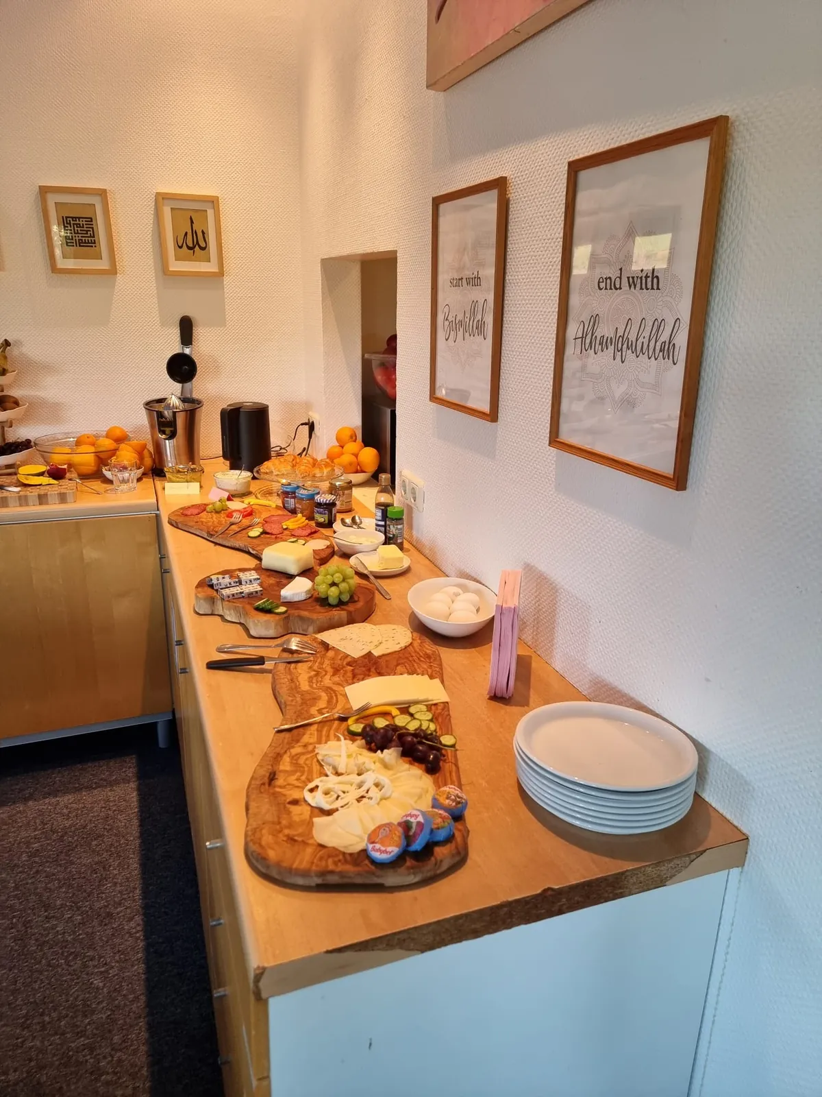 Frühstücksbuffet mit Obst und Käseplatten unter Bildern mit den Schriftzügen »start with Bismillah« und »end with Alhamdulillah«.